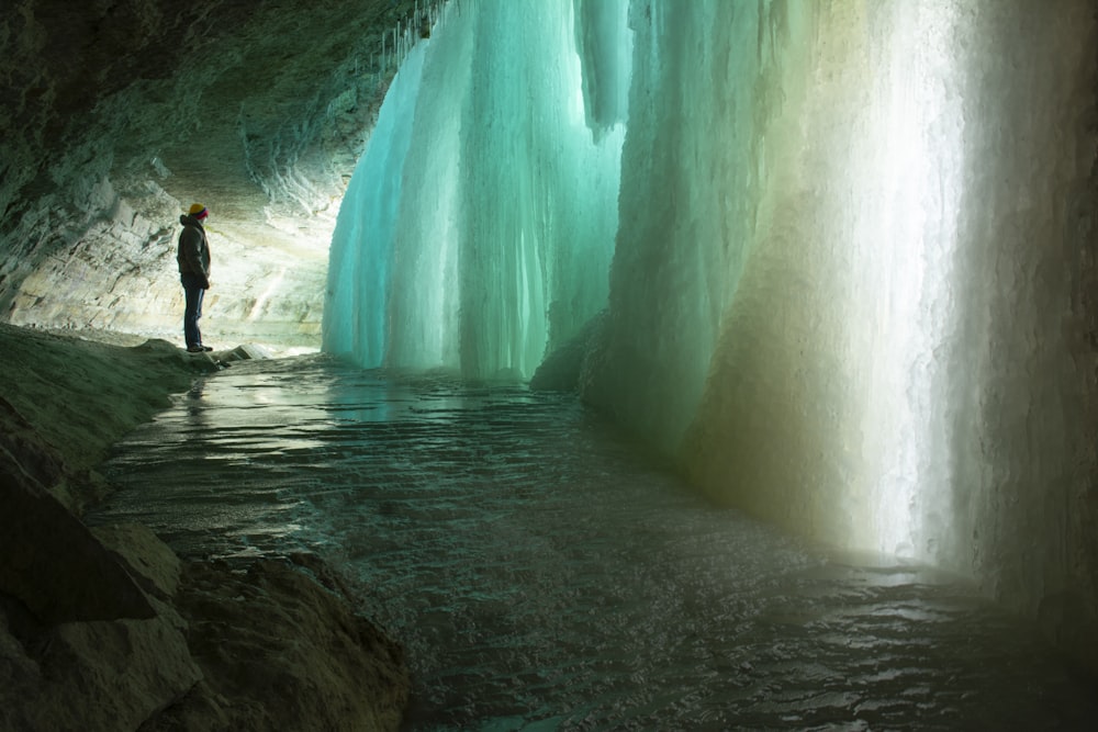 a man standing in a cave next to a waterfall