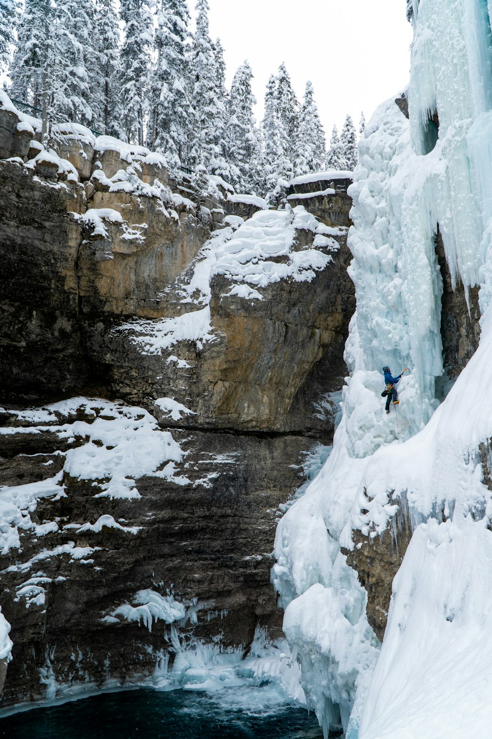 a person climbing up a snowy cliff next to a waterfall
