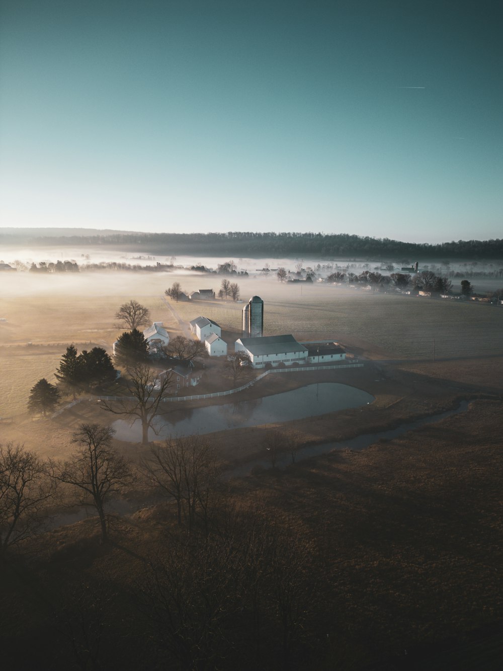 a foggy landscape with a farm and a lake