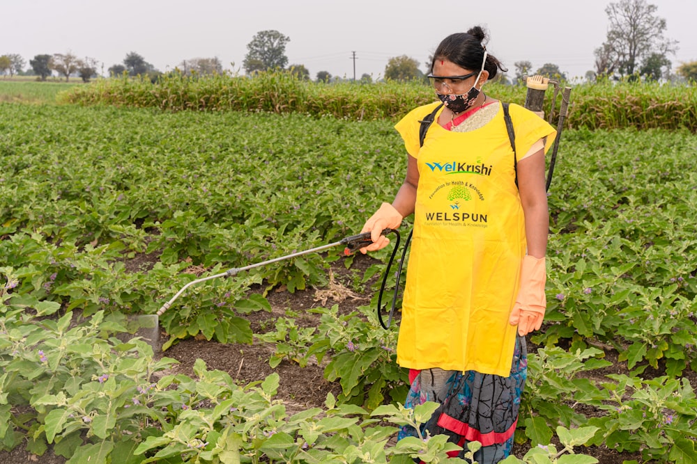 a woman in a yellow apron is spraying water on a field