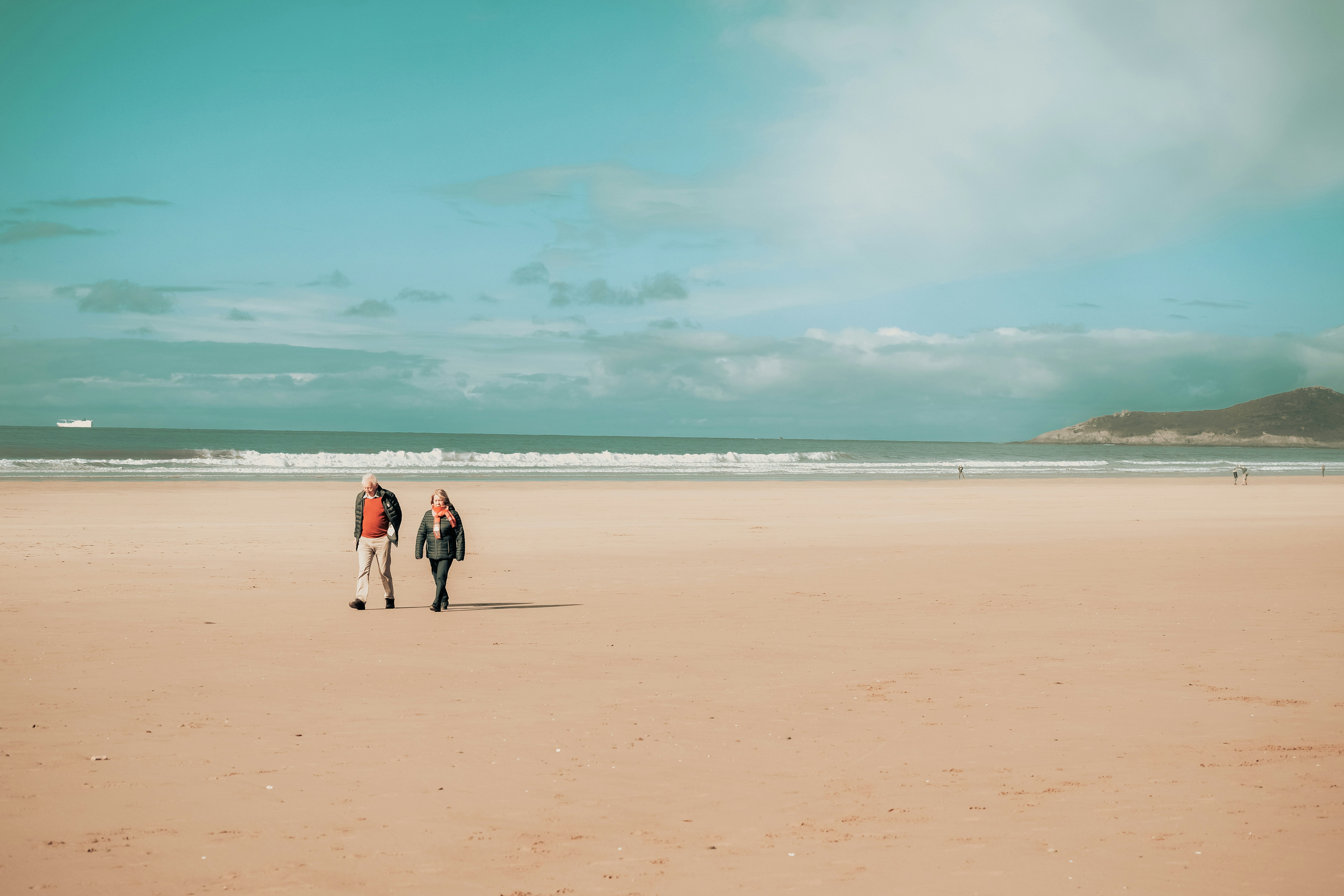 two people walking on a beach near the ocean