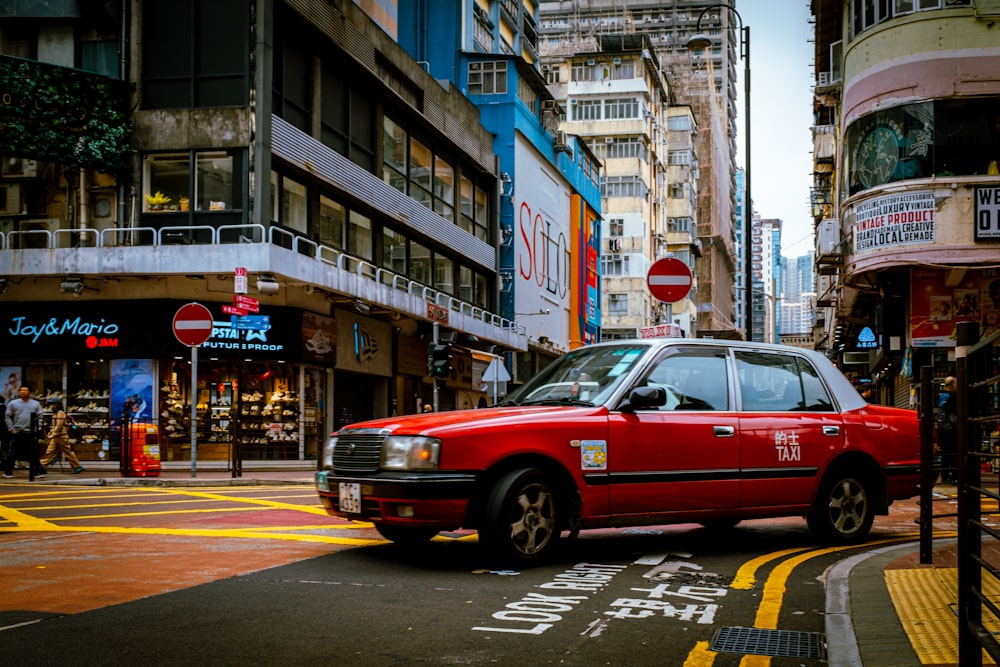 a red car driving down a street next to tall buildings