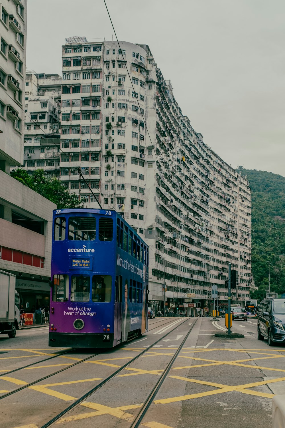 a blue double decker bus driving down a street next to tall buildings