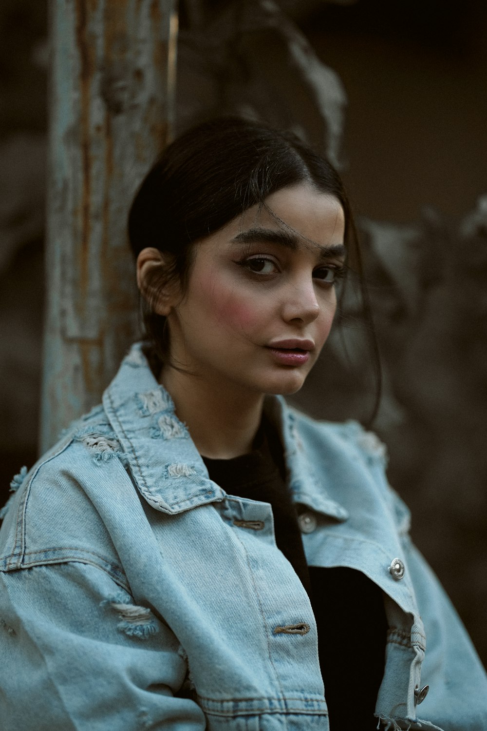 a woman in a denim jacket leaning against a tree