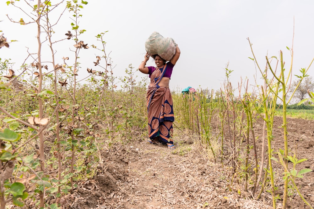 a woman carrying a sack over her head in a field