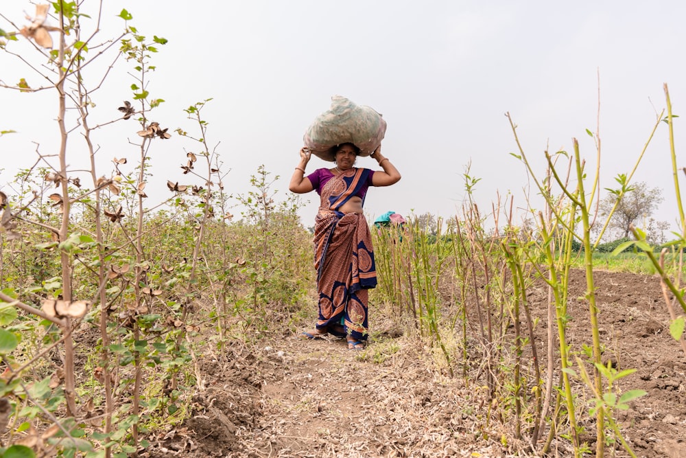 uma mulher caminhando por um campo carregando um saco na cabeça