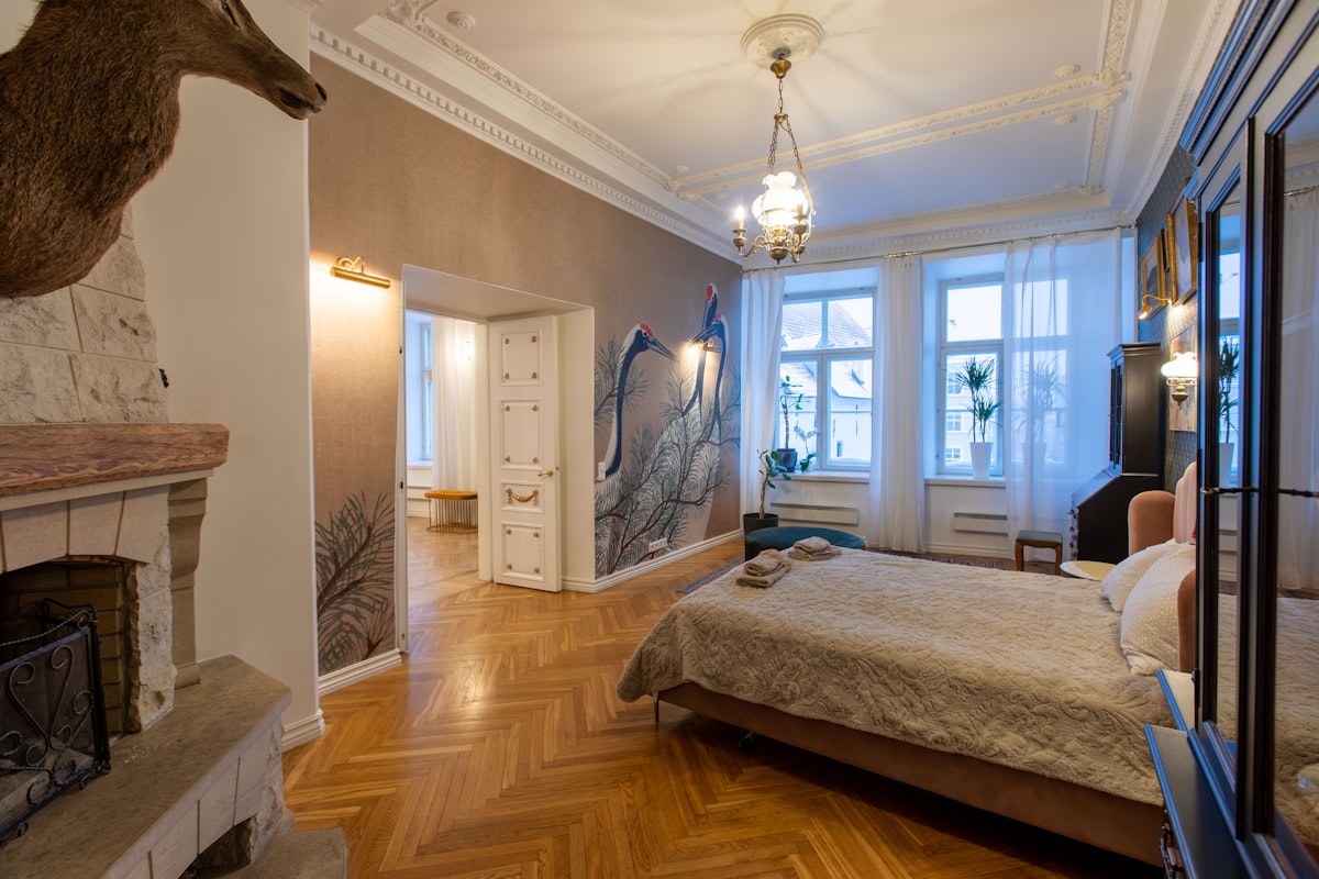 Dormitorio con una pared empapelada con un papel pintado de patrón de grullas y vegetación, junto a una chimenea y piso de parquet