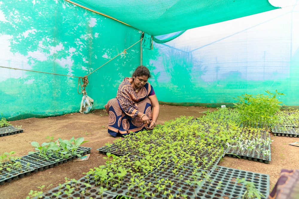 a woman kneeling down in front of a bunch of plants