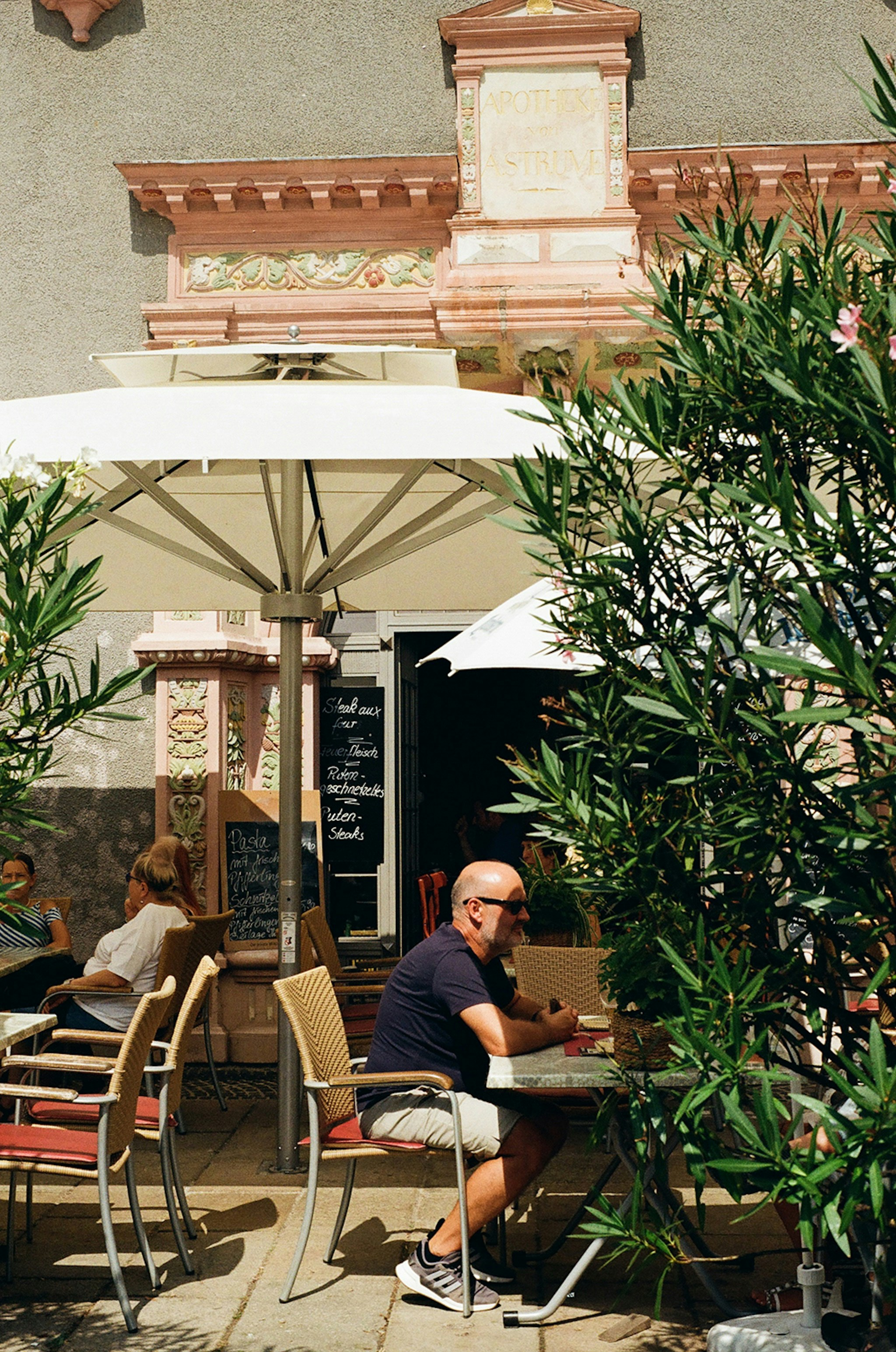 Man eating alone at outdoor table in rain, umbrella leaning against chair, completely at peace