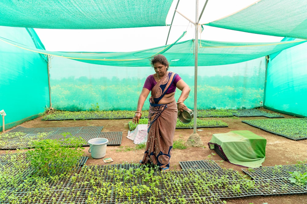 a woman standing in a greenhouse holding a bucket