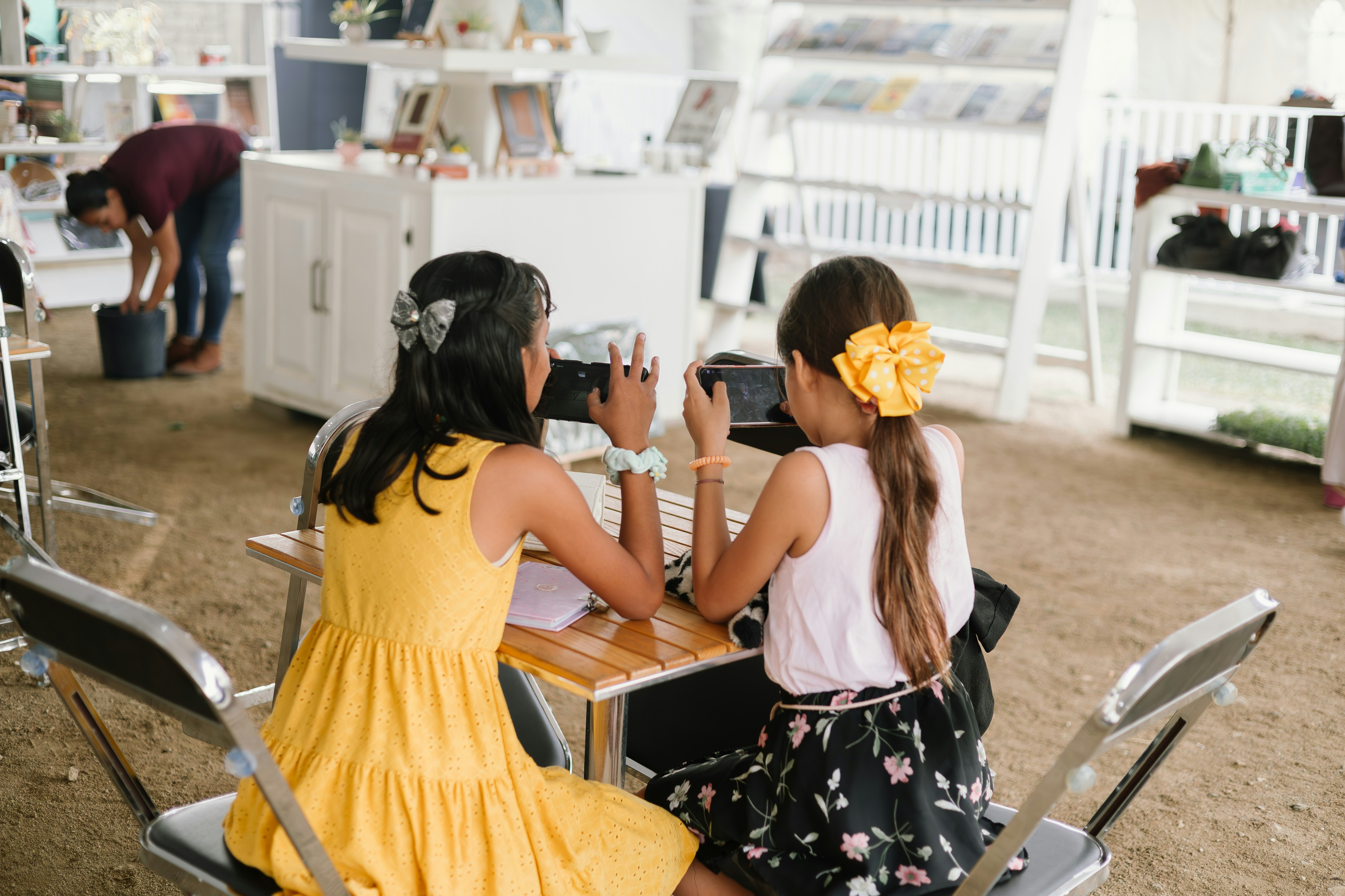 two little girls sitting at a table taking pictures