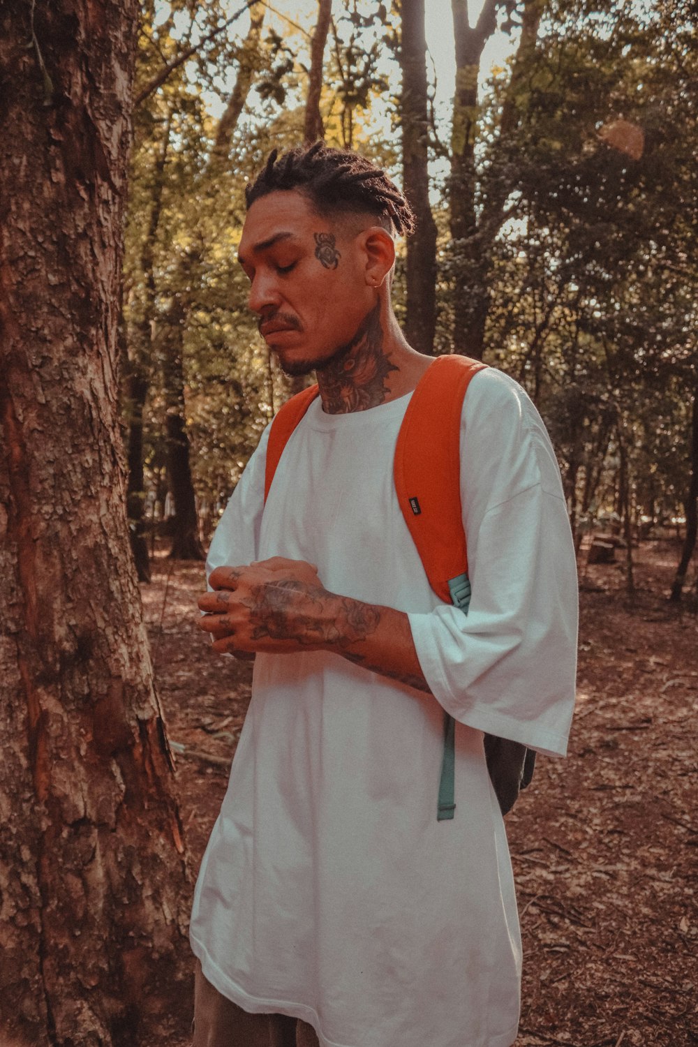 a man with tattoos standing next to a tree