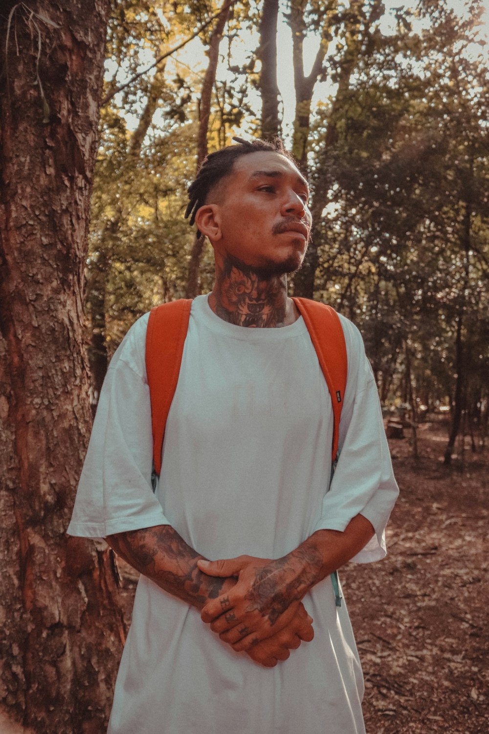 a man with tattoos standing next to a tree