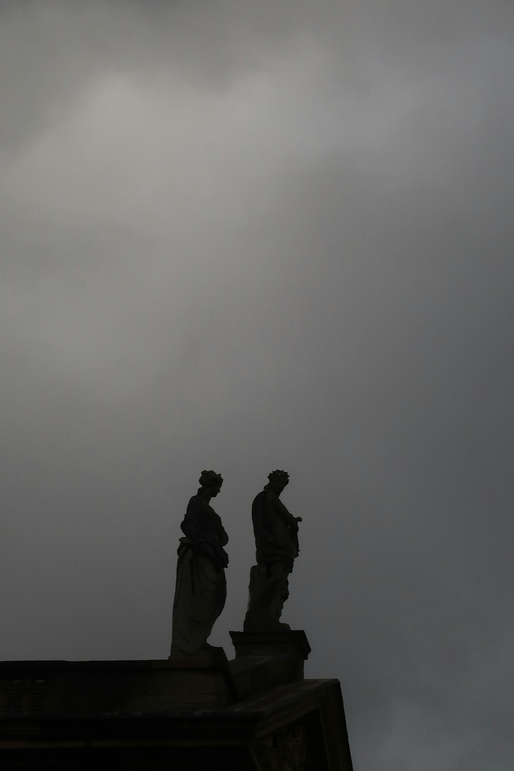 Deux statues au sommet d’un bâtiment sous un ciel nuageux