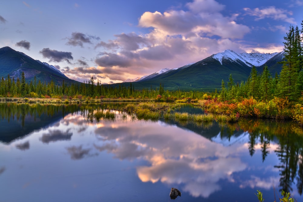 a lake surrounded by trees and mountains under a cloudy sky