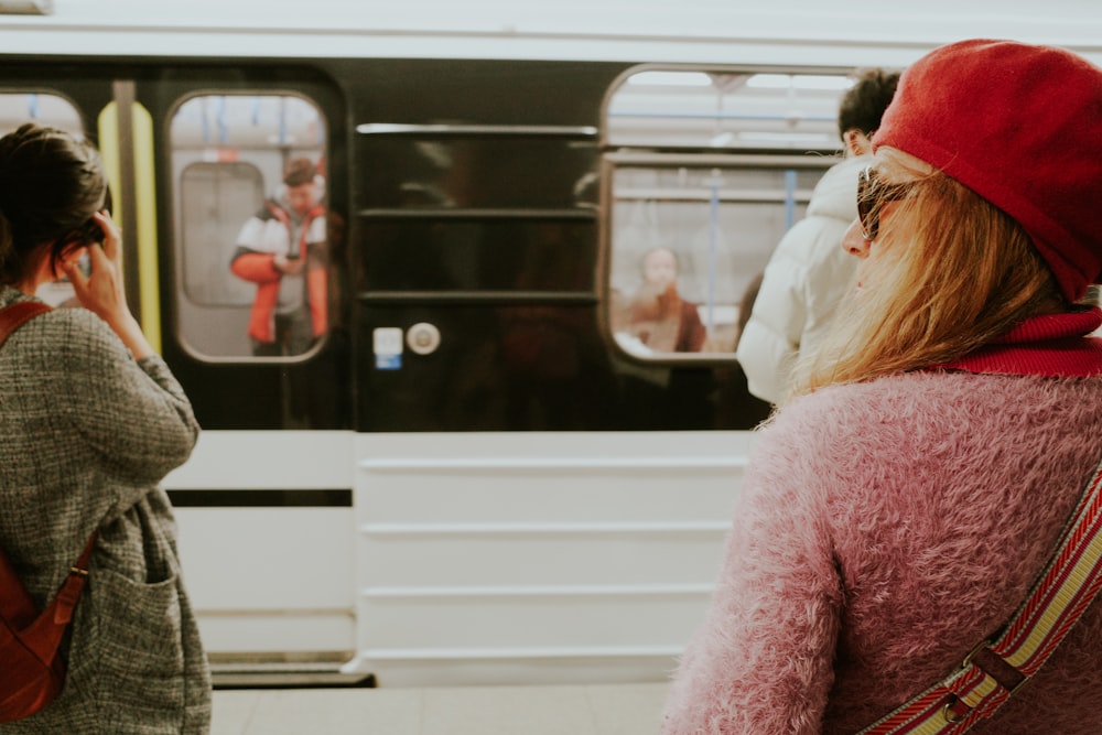 a woman standing next to a train while talking on a cell phone