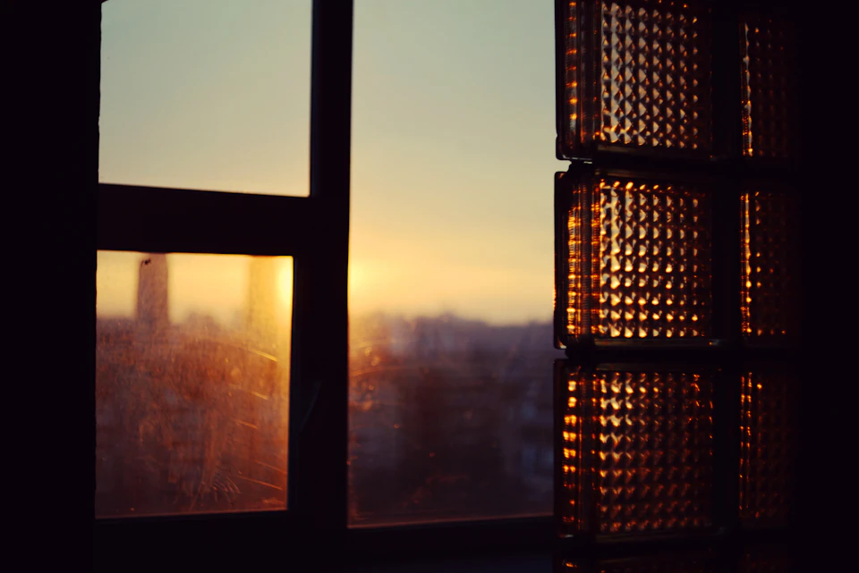 Window with black bars framing a city skyline at sunset with warm orange glow