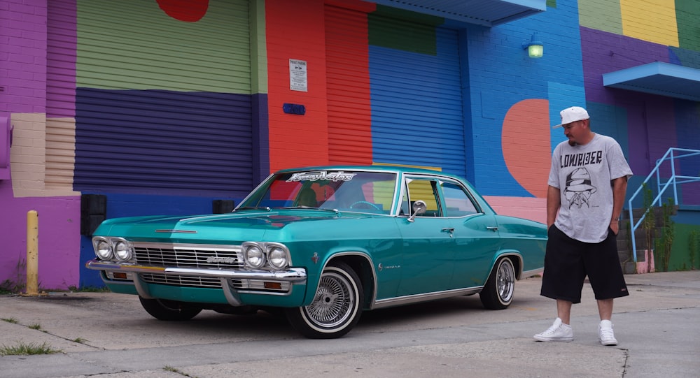 a man standing next to a car in front of a colorful building