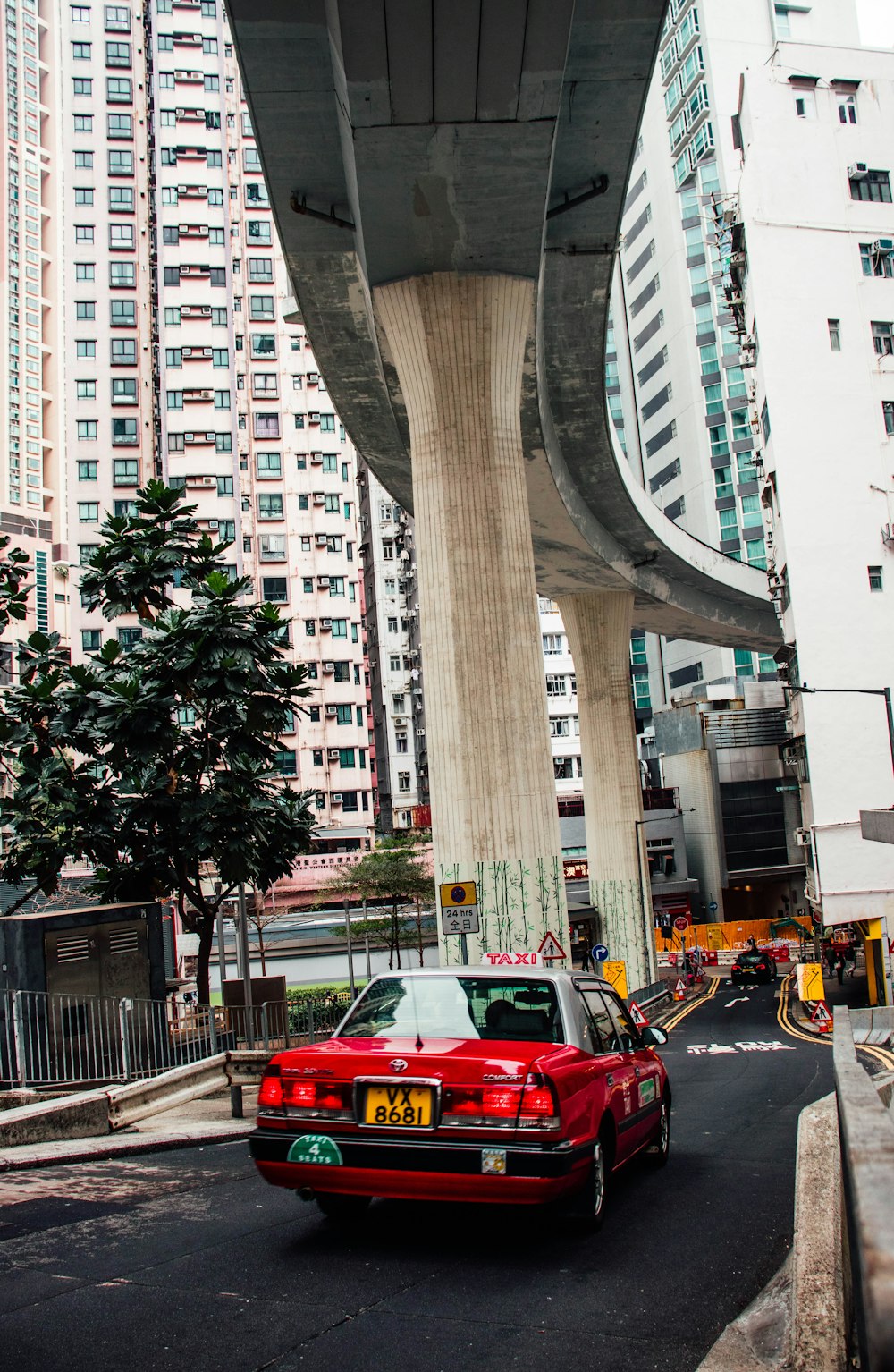 a red car driving under a bridge in a city