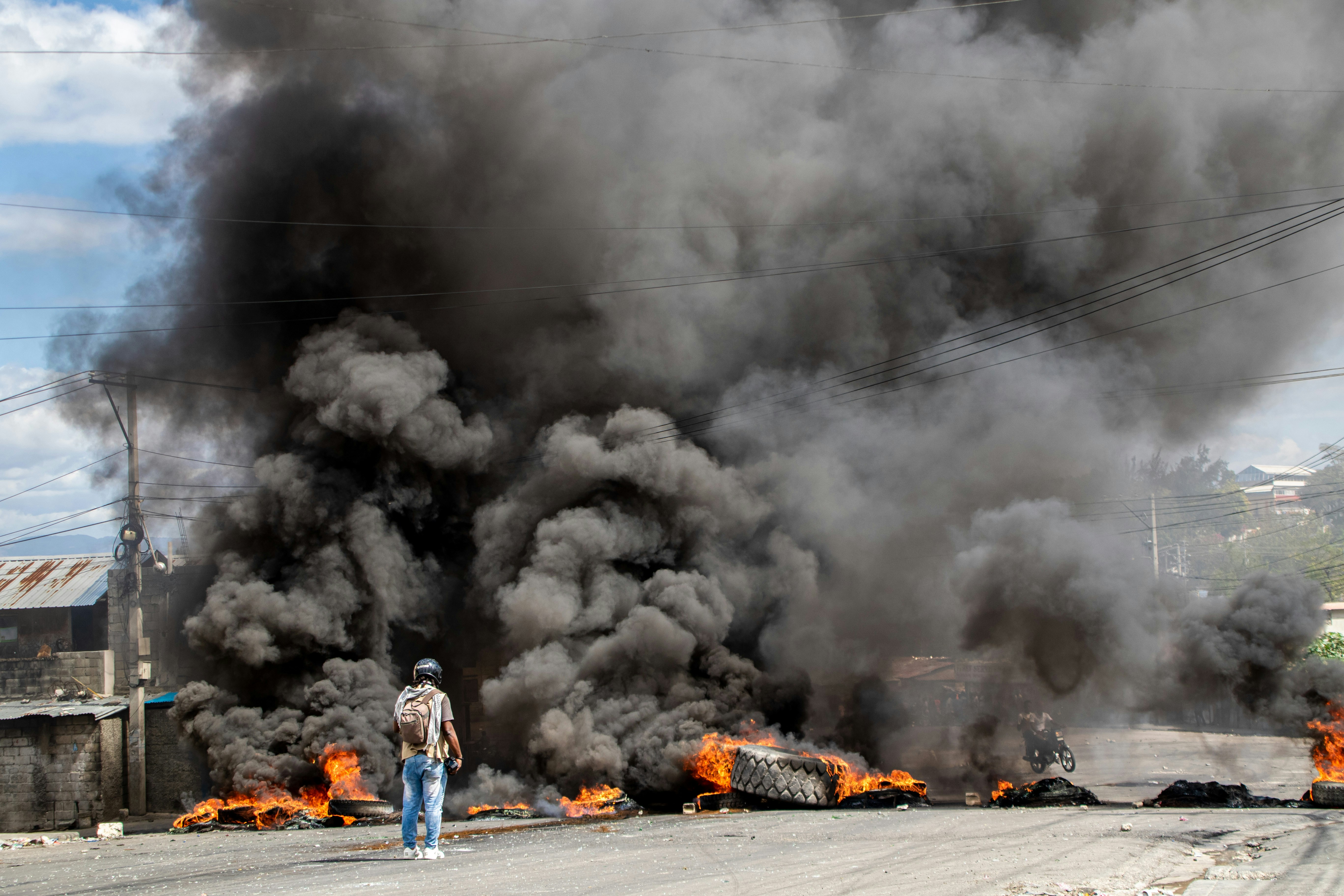 “Reporter captures video in front of burning barricade in Haiti during protest.”