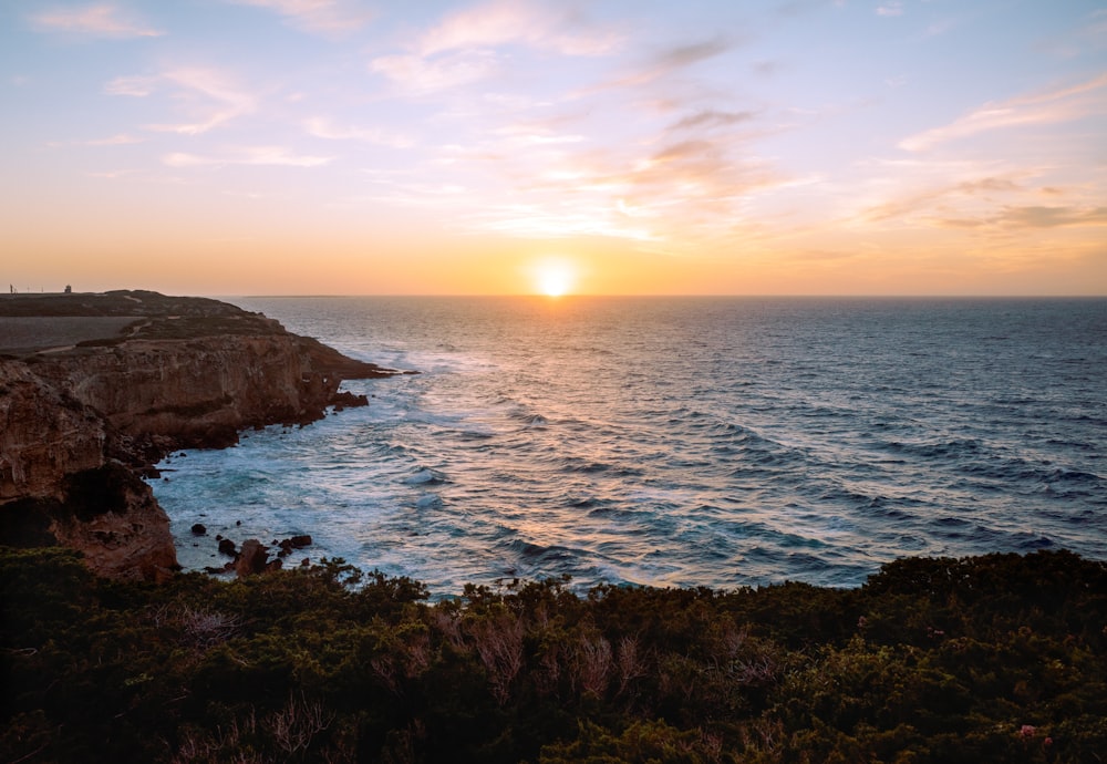 the sun is setting over the ocean on a cliff