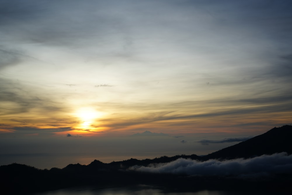 the sun is setting over a mountain with clouds in the foreground