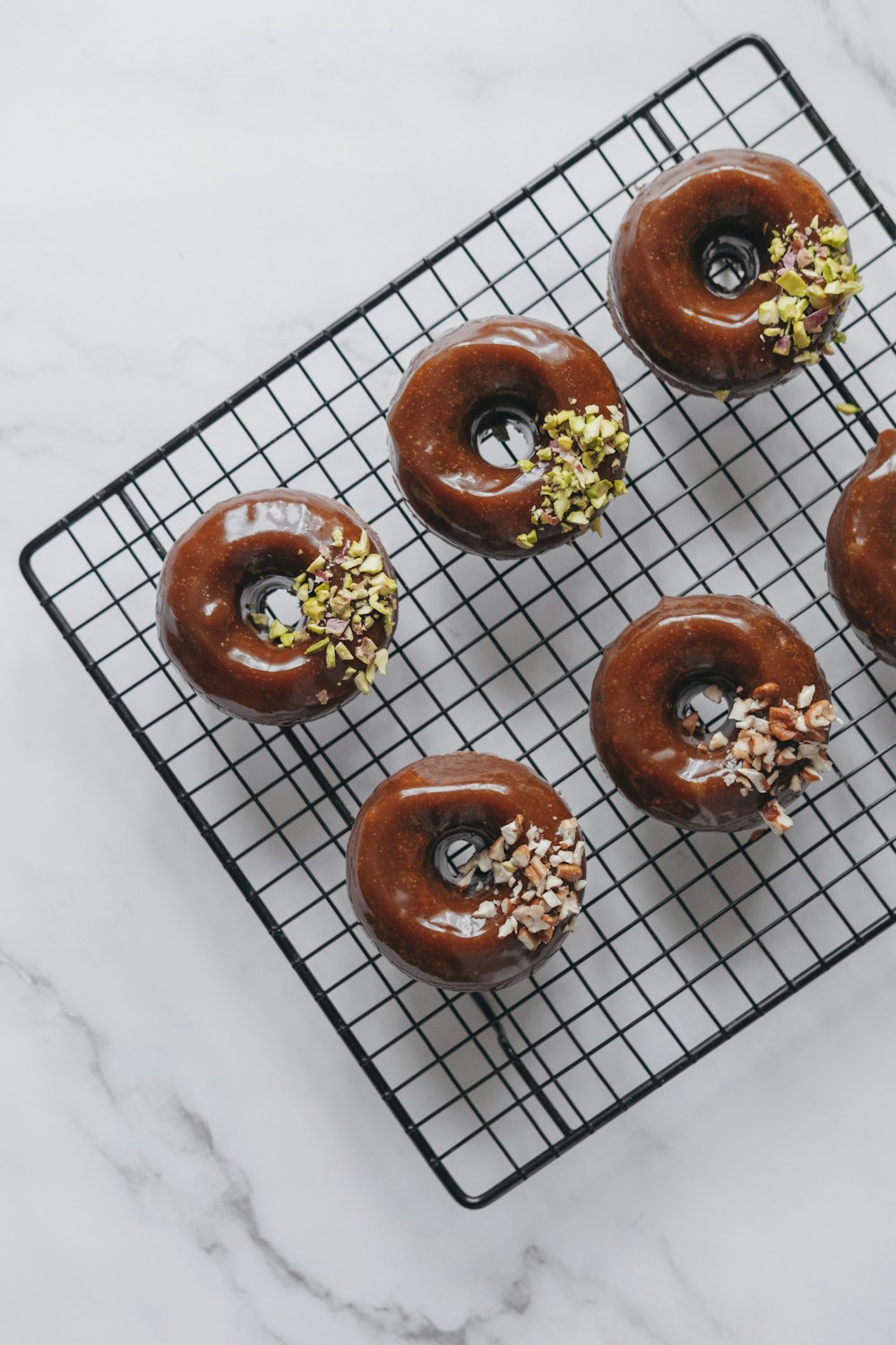 four chocolate donuts on a cooling rack on a marble counter
