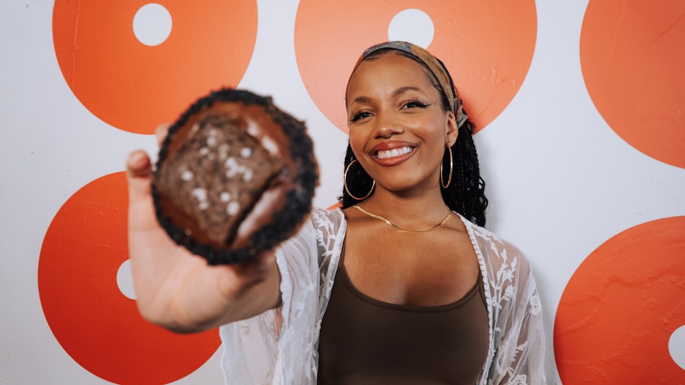 a woman holding a chocolate donut in front of a wall