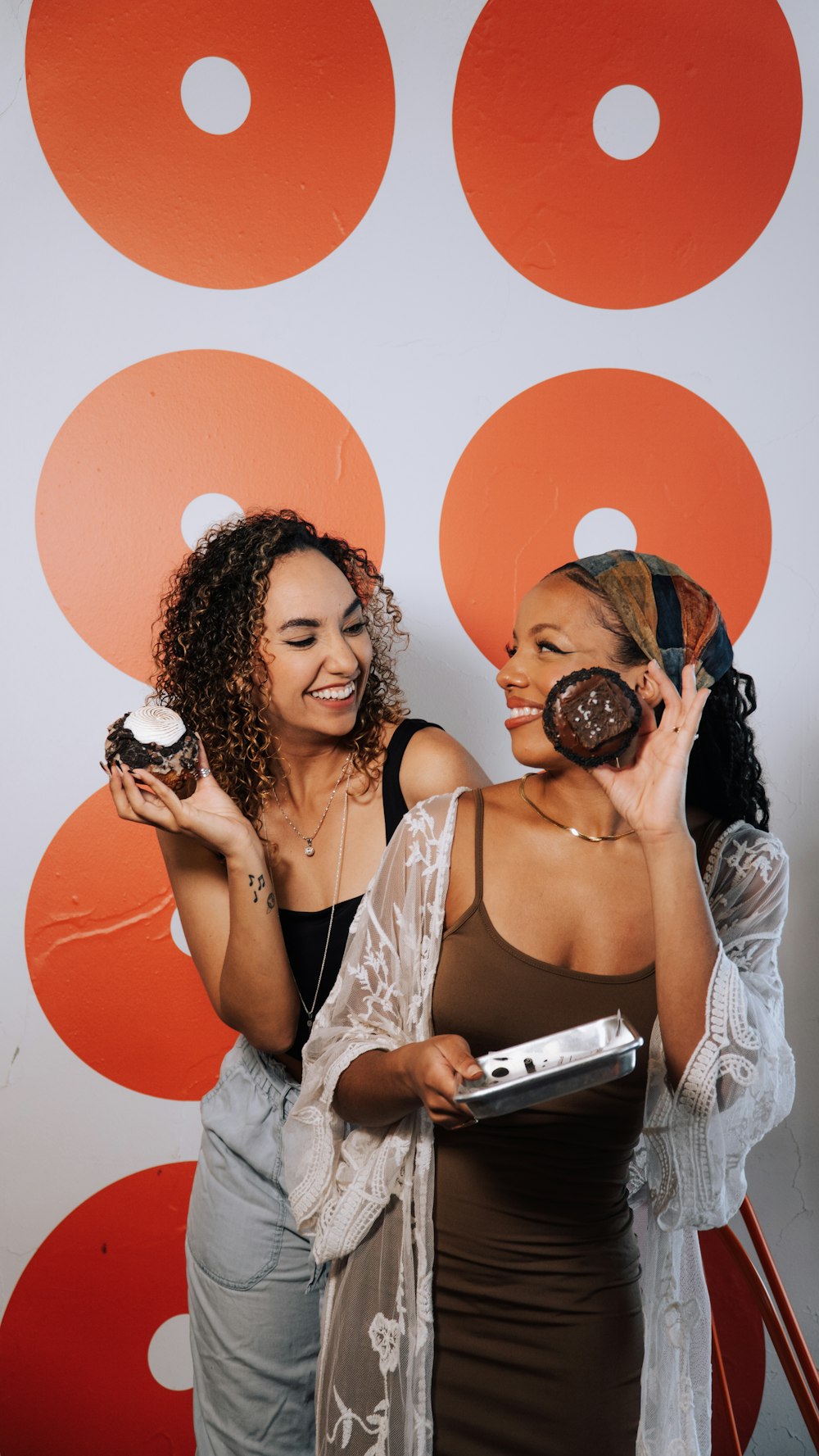 two women standing next to each other holding donuts