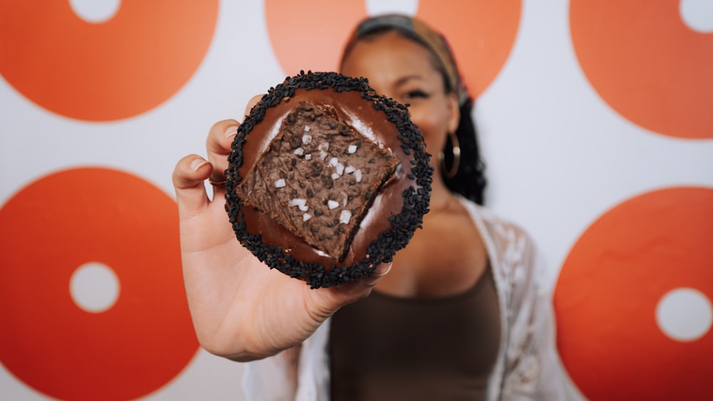 a woman holding up a chocolate donut in front of a wall