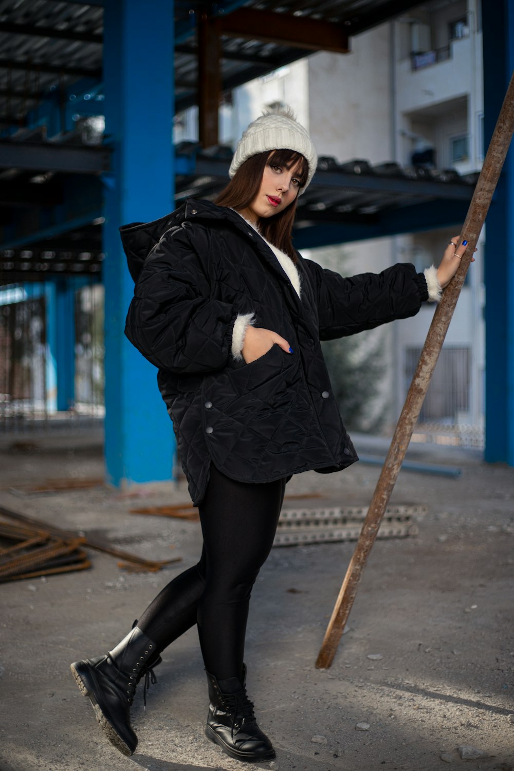 a woman in a black coat and hat holding a stick