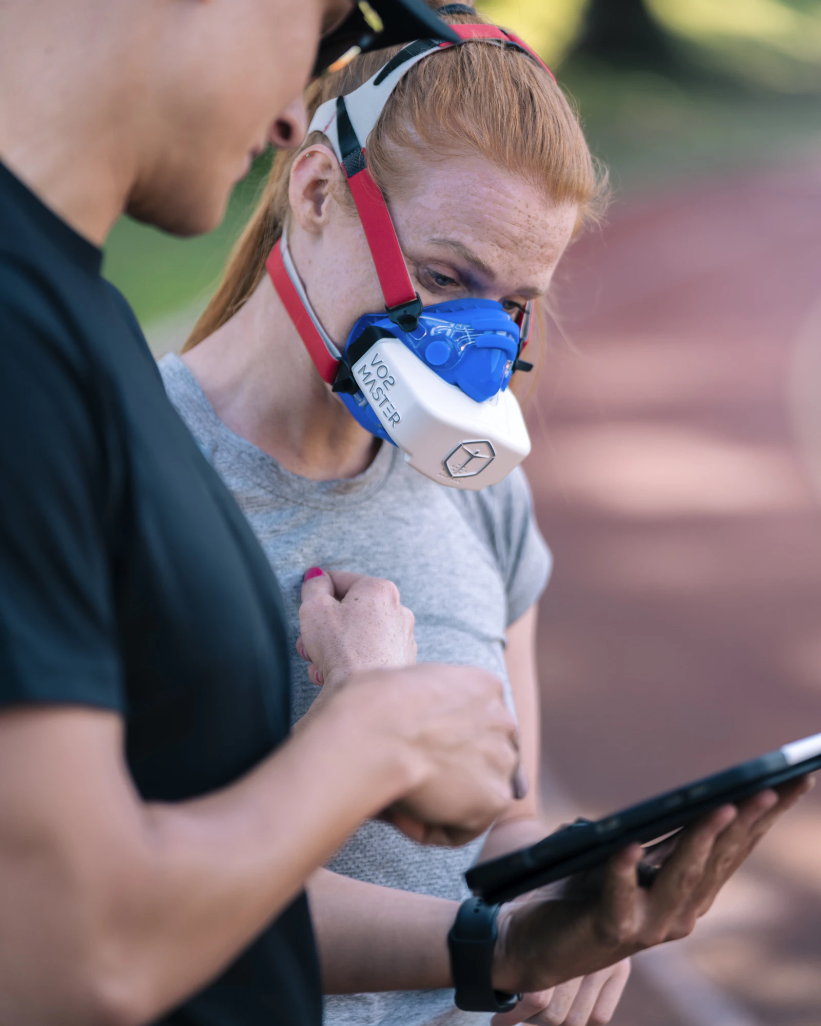A woman wearing a gas-exchange mask stands beside a tester reading results from a tablet