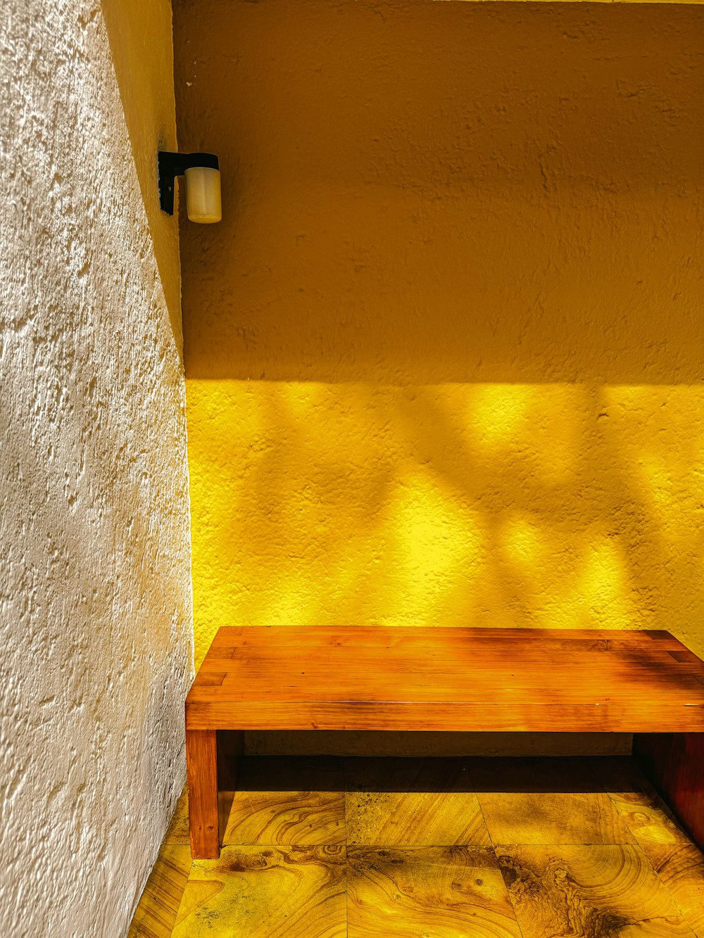 a wooden bench sitting in front of a yellow wall