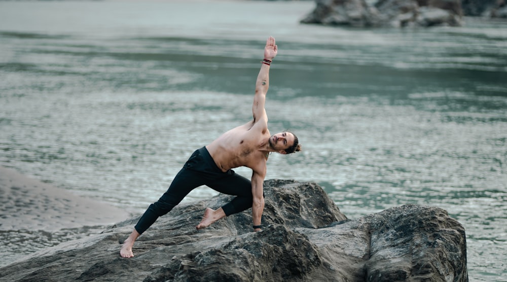 ein Mann, der eine Yoga-Pose auf einem Felsen am Wasser macht