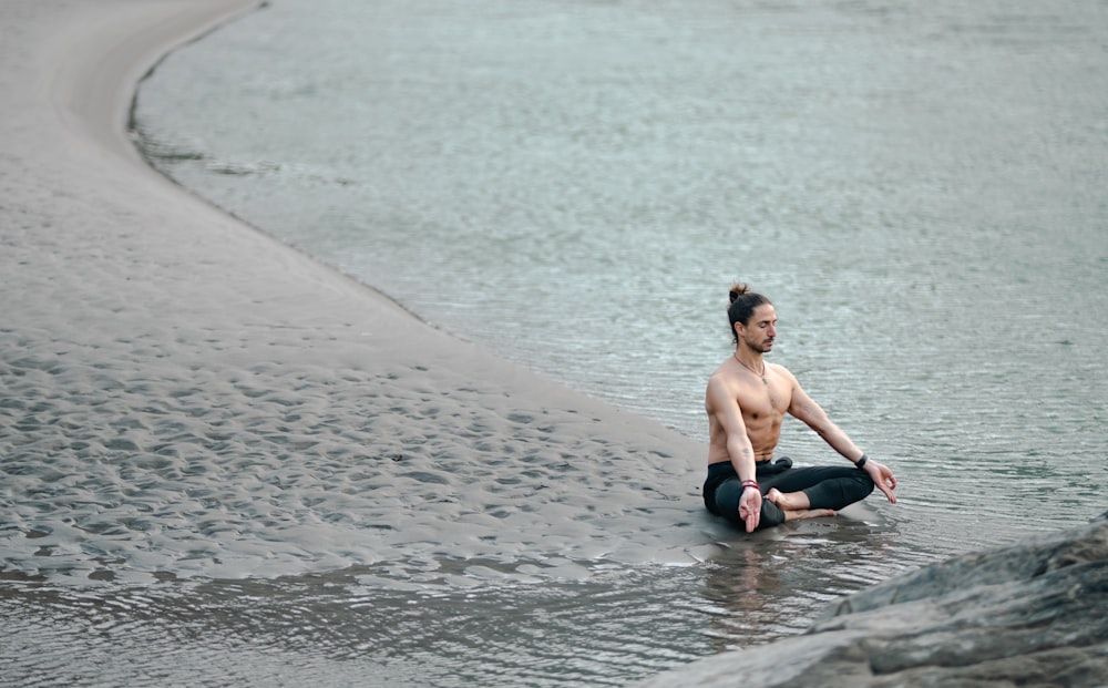um homem sem camisa sentado à beira de um corpo de água