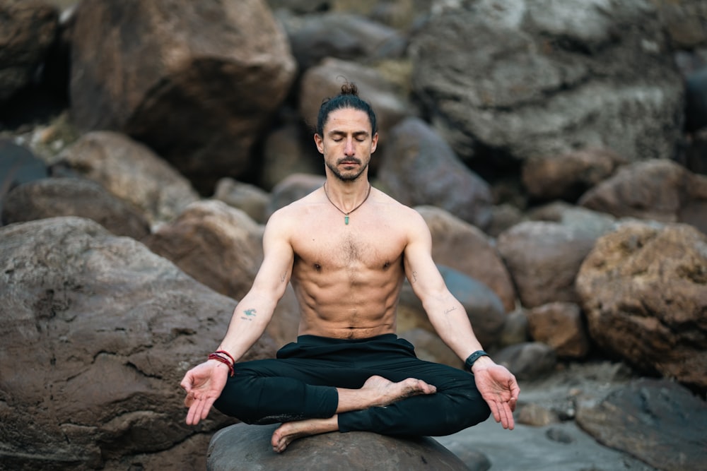 un homme assis sur un rocher en train de faire du yoga