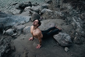 a shirtless man laying on a rocky beach
