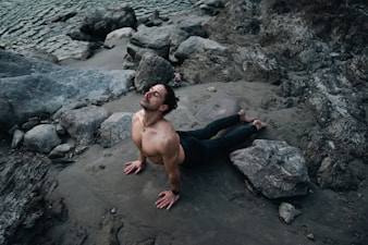a shirtless man laying on a rocky beach