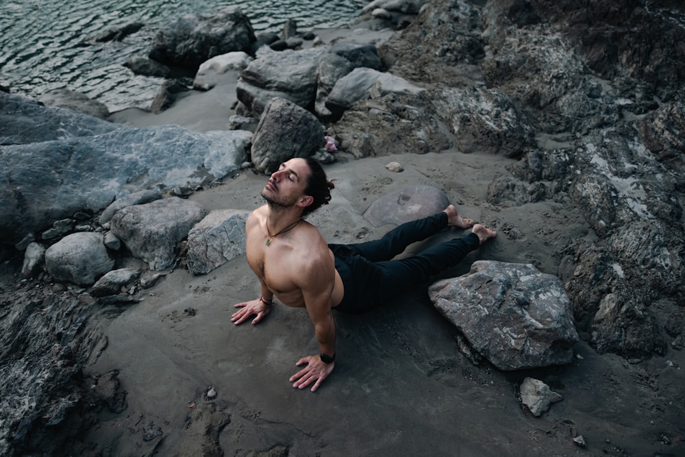 a shirtless man laying on a rocky beach