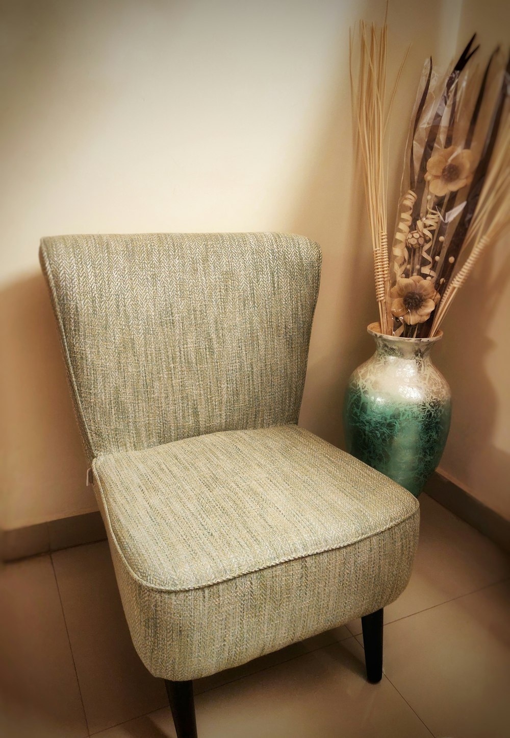 a chair next to a vase with a plant in it