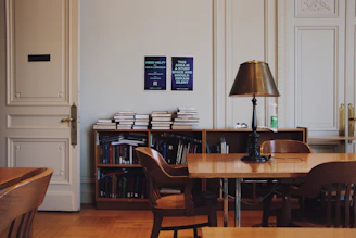 a room with a table, chairs, bookshelf and a lamp
