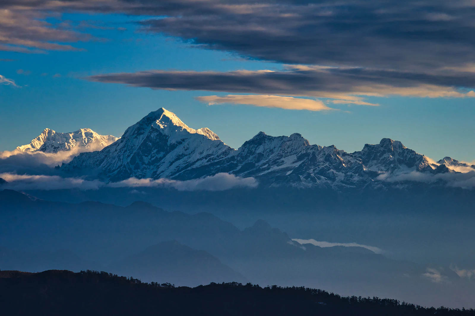 Snow peaks of the Kanchenjunga range above layered blue ridges and cloud at dawn, seen from Sandakphu