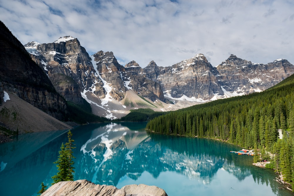 a lake surrounded by trees and mountains under a cloudy sky