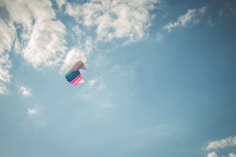 a colorful kite flying through a cloudy blue sky