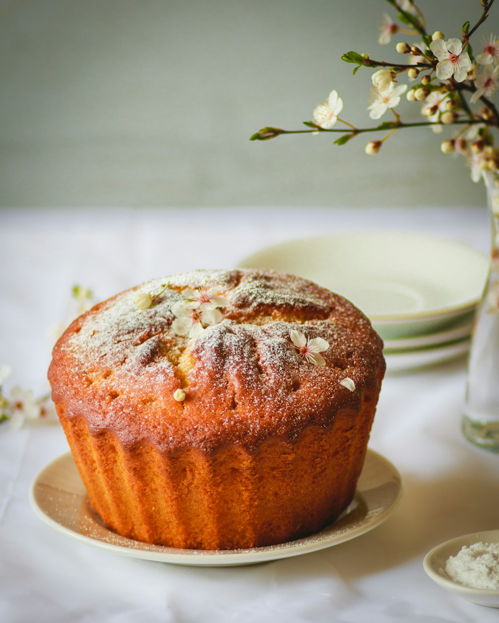 a muffin sitting on a plate next to a vase of flowers