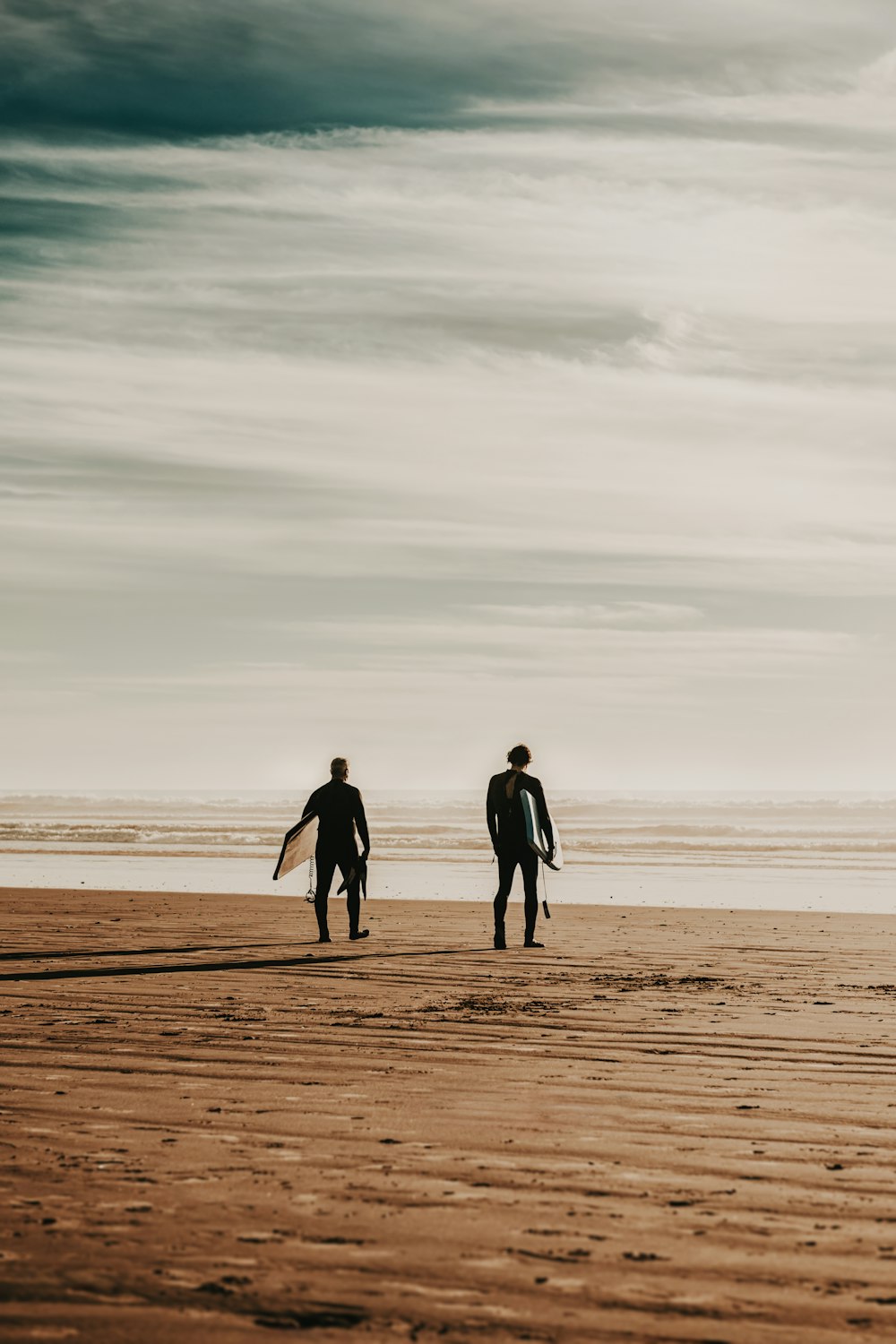 Zwei Surfer, die mit ihren Brettern am Strand spazieren gehen