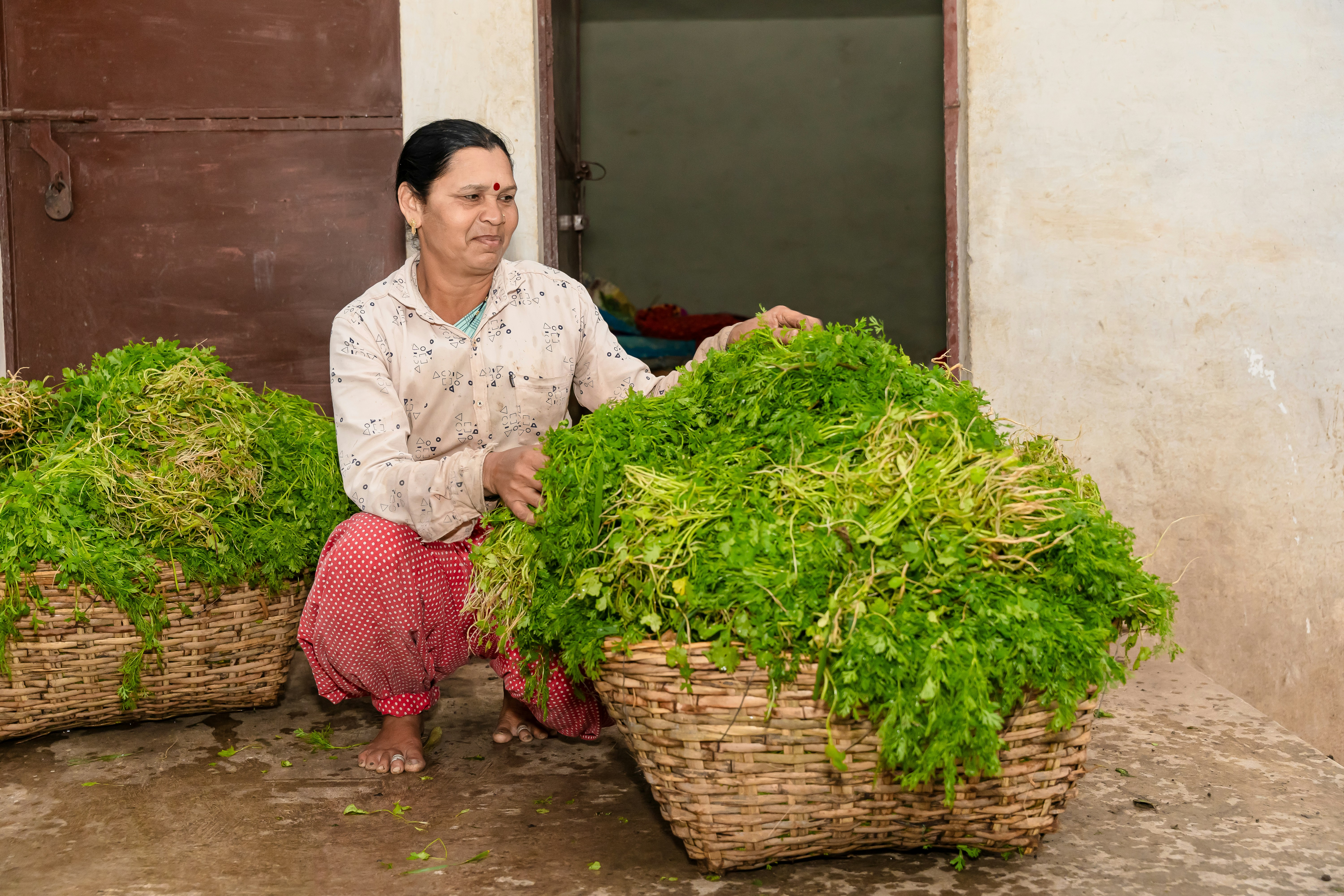 a woman kneeling down next to baskets filled with greens