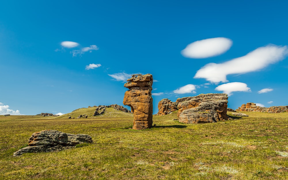 a rock formation in a grassy field under a blue sky