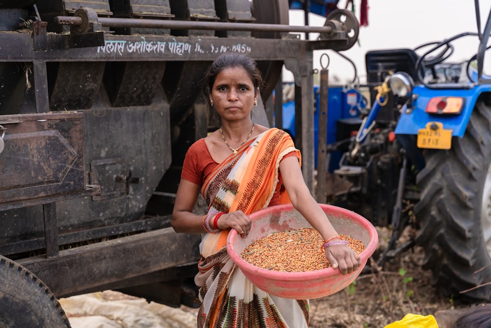 a woman holding a bowl of grain in front of a tractor