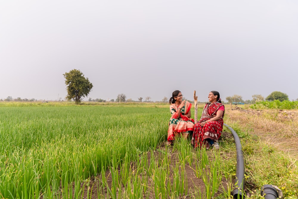a couple of women sitting on top of a lush green field
